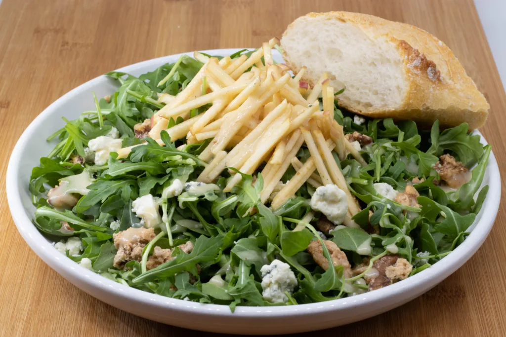 Arugula salad topped with apple matchsticks, blue cheese and candied walnuts, served with a slice of baguette