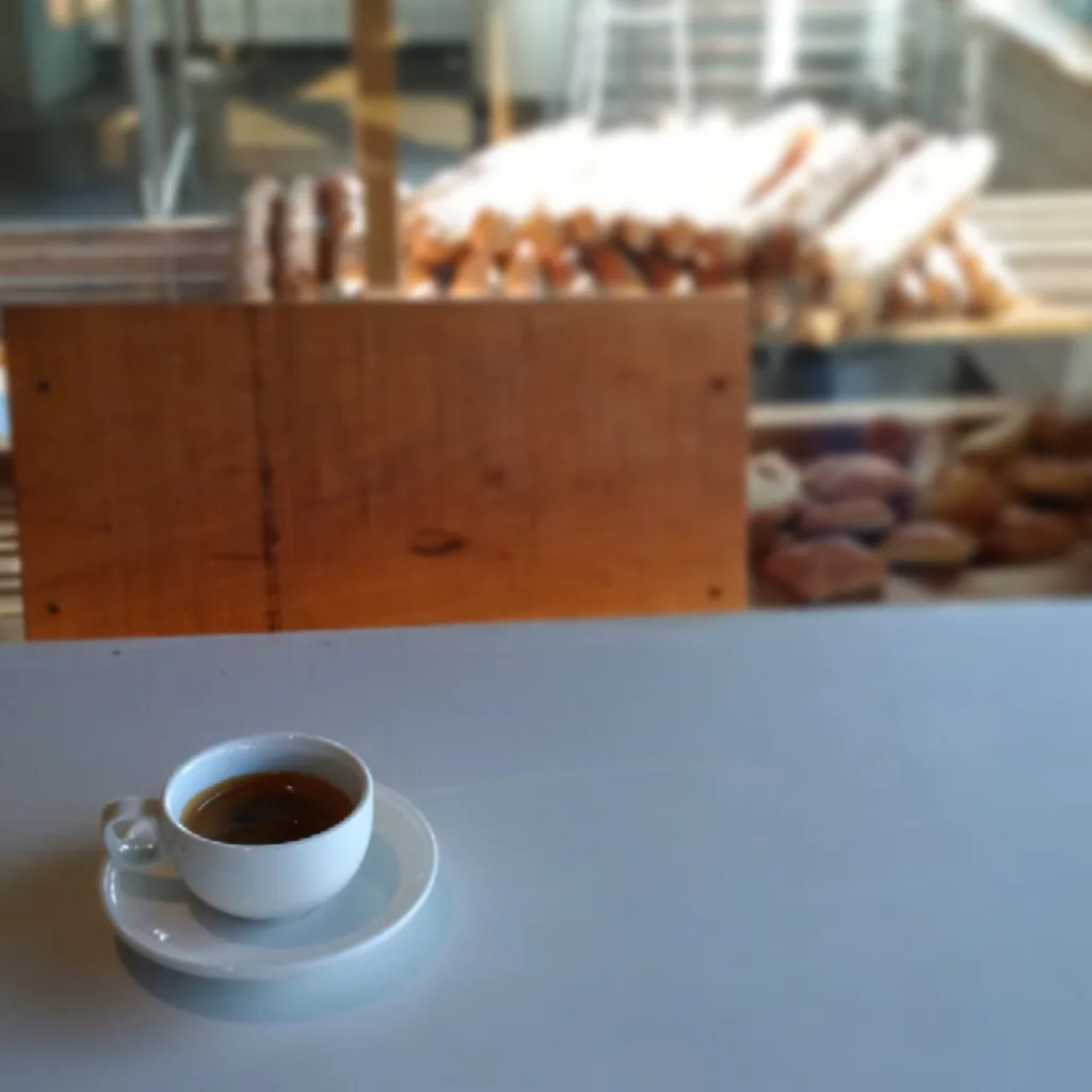 An espresso cup on the counter in front of the bread shelves