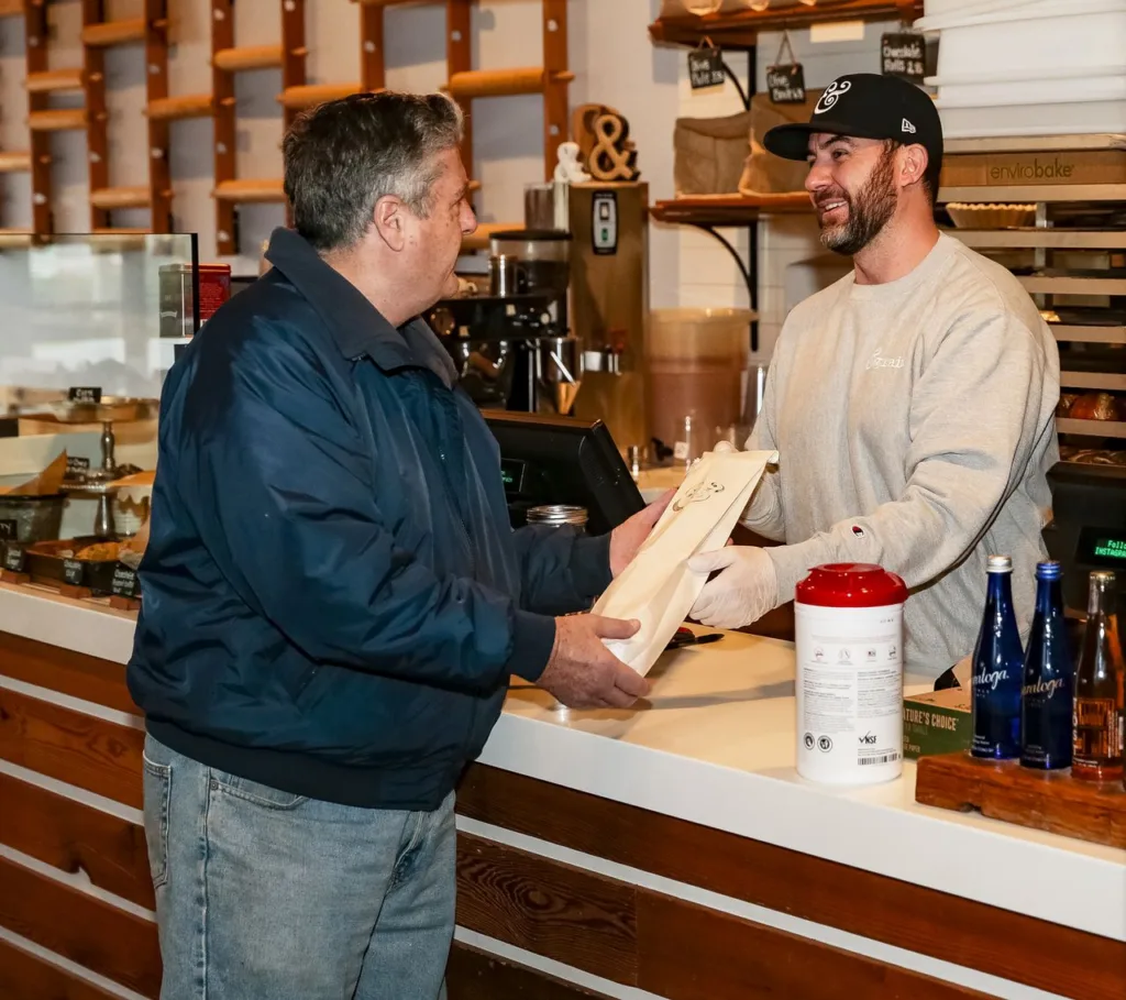 An &grain owner handing a loaf of bread to a customer at the counter