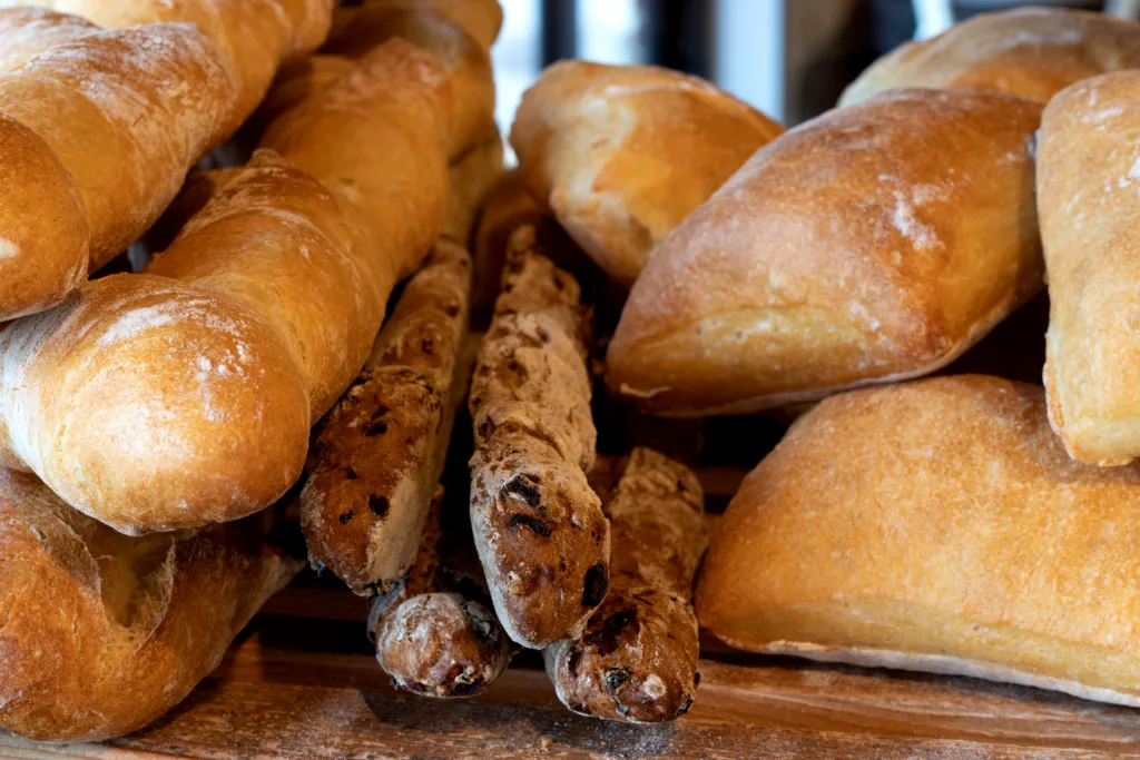 Baguettes, olive sticks and ciabatta rolls stacked on a wooden board at &grain